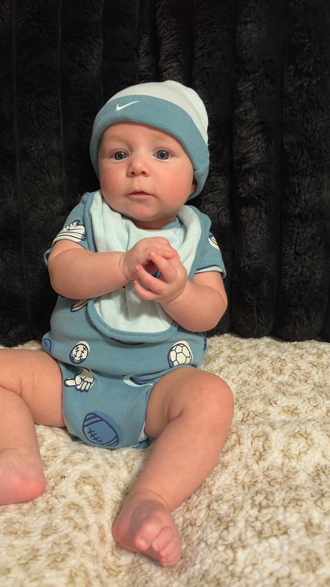 Amir joined the competition — help win amazing prizes! baby, infant, blue_hat, blue_onesie, sports_pattern, hands_clasped, sitting, blanket, cozy, indoor, portrait, cute, child, soft_texture, curious, headwear, foot, skin, baby_clothing, expression