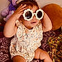 Alorah is registered to the contest to win money with this photo: toddler, child, sunglasses, flower_shaped, plush_toy, stuffed_animal, purple, blanket, patterned, cushion, indoor, cute, playful, hands_up, baby_clothes, floral_pattern, smiling, seated, person, home