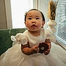 baby, child, girl, white_dress, cookie, chair, indoor, window, curtain, vase, flower_arrangement, adorable, portrait, cute, sitting, bow, earrings, happy, young, face