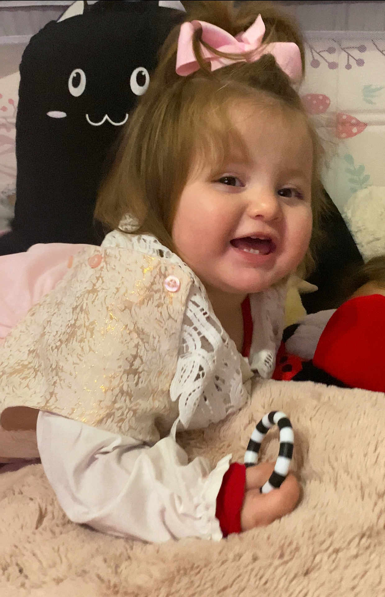 Maya is registered to the contest to win money with this photo: toddler, child, baby, pink_bow, smiling, toy, plush_toy, blanket, soft_texture, bedroom, cute, happy, indoor, white_clothing, red_clothing, face, hand, playful, closeup, portrait
