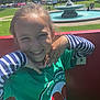 Malak joined the competition — help win amazing prizes! child, smiling, green_shirt, striped_sleeves, necklace, outdoor, park, fountain, trees, sunny, people, grass, daytime, happy, portrait, casual_clothing, playful_pose, young_girl, background, nature