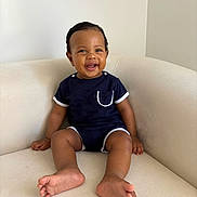 Ilyes participe au concours pour gagner de l'argent avec cette photo : baby, toddler, smiling, sitting, couch, onesie, navy_blue, white_trim, happy, child, indoors, portrait, cute, infant, skin, foot, hand, face, minimalist, background