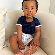 Ilyes participe au concours pour gagner de l'argent avec cette photo : adorable, armchair, baby, bare_feet, big_eyes, child, couch, curly_hair, cushion, hands, indoor, minimal_background, navy_shirt, portrait, sitting, smile, toddler, toes, warm_skin_tone, white_shorts