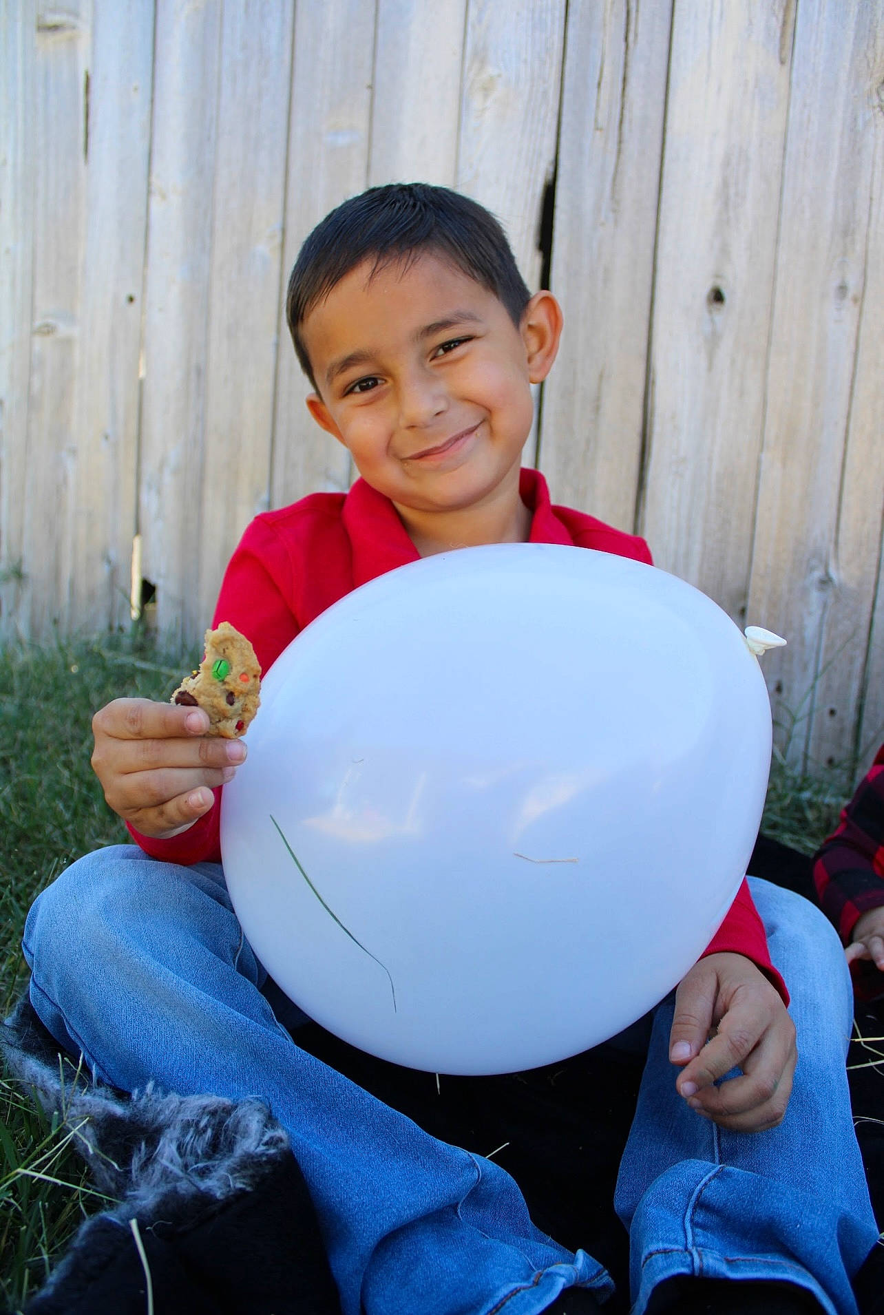 Gabriel is registered to the contest to win money with this photo: automotive_wheel_system, ball, balloon, child, clothing, electric_blue, facial_expression, fun, grass, happy, helmet, joy, person, personal_protective_equipment, plant, play, shorts, sitting, sleeve, smile