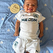 Tony a rejoint le concours — aidez-le/la à gagner de superbes lots ! baby, infant, smiling, white_clothing, sportswear, blue_blanket, heart_pattern, wooden_plaque, text, two_months, lying_down, happy, cute, infant_boy, bracelet, tongue_out, indoor, portrait, child, person