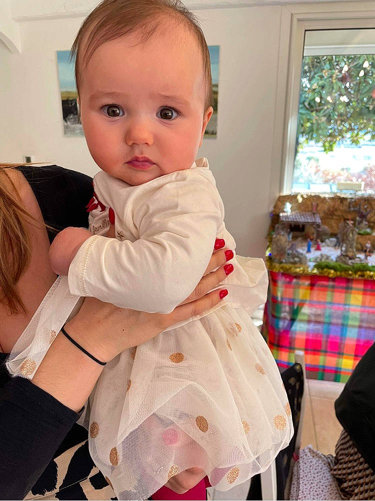 Laureline participe au concours pour gagner de l'argent avec cette photo : abdomen, baby, baby_products, baby_toddler_clothing, child, dress, event, formal_wear, gesture, happy, iris, linens, pattern, person, plaid, product, room, sitting, sleeve, tartan