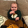 Loan participe au concours pour gagner de l'argent avec cette photo : baby, infant, smiling, blue_eyes, chubby_cheeks, green_sweater, fox_motif, brown_pants, black_socks, mustard_blanket, couch, striped_cushion, throw_pillow, indoor, sitting, portrait, cute, cozy, hand_gesture, wall_texture