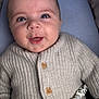 baby, infant, face, smiling, knitted_sweater, buttons, blue_eyes, toy, cushion, close_up, happy, child, person, portrait, soft_lighting, indoor, cute, newborn, hand, cozy