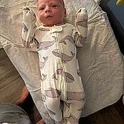 Jett is registered to the contest to win money with this photo: baby, infant, onesie, whale_pattern, blanket, lying_down, indoor, wooden_floor, cute, newborn, sleepwear, person, small_hands, footed_pajamas, facial_expression, curious, soft_texture, home, child, baby_clothes