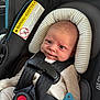 baby, car_seat, infant, seat_belt, pacifier, striped_pillow, black_straps, beige_clothing, face, head_support, child, safety, cute, indoors, closeup, newborn, expression, secure, comfort, car_interior