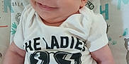 Dougie is registered to the contest to win money with this photo: baby, infant, smile, onesie, clothing, face, arm, lying_down, blanket, pattern, cute, child, person, happy, closeup, skin, head, expression, babywear, background