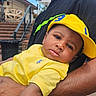 baby, child, yellow_hat, yellow_shirt, person, outdoor, arm, skin, face, headwear, holding, adult, stairs, blurred_background, curious, casual_clothing, daylight, portrait, closeup, expression