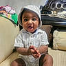 baby, child, smiling, clapping, hat, striped_shirt, couch, cushion, pillow, indoors, happy, person, infant, seated, cute, plush, furniture, home, portrait, young