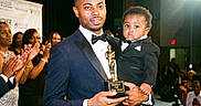 D'Montae joined the competition — help win amazing prizes! man, child, tuxedo, award, trophy, stage, applause, crowd, celebration, event, formal_wear, father, son, black_suit, smile, indoor, people, lighting, portrait, ceremony