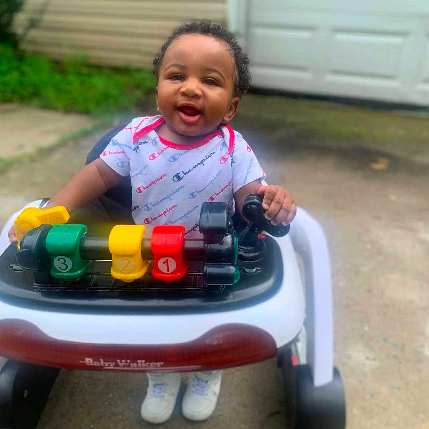 D'Montae is registered to the contest to win money with this photo: baby, child, walker, toy, outdoor, smiling, happy, person, clothing, footwear, concrete, building, garage, window, greenery, curb, plastic, hands, face, shoes