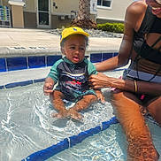 D'Montae joined the competition — help win amazing prizes! adult, child, family, fun, hand, leg, outdoor, pool, recreation, sitting, skin, smile, splash, summer, sunny, swimsuit, toddler, water, water_reflection, yellow_cap