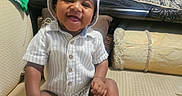 D'Montae joined the competition — help win amazing prizes! baby, smiling, sitting, indoor, hat, striped_clothing, white_shoes, couch, pillow, bed, happy, child, infant, home, furniture, cute, portrait, person, relaxed, comfortable