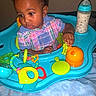 baby, child, walker, toy, bottle, milk, plaid_shirt, indoor, curious, infant, colorful, plastic_toy, seat, blanket, portrait, young_child, face, hand, playtime, person