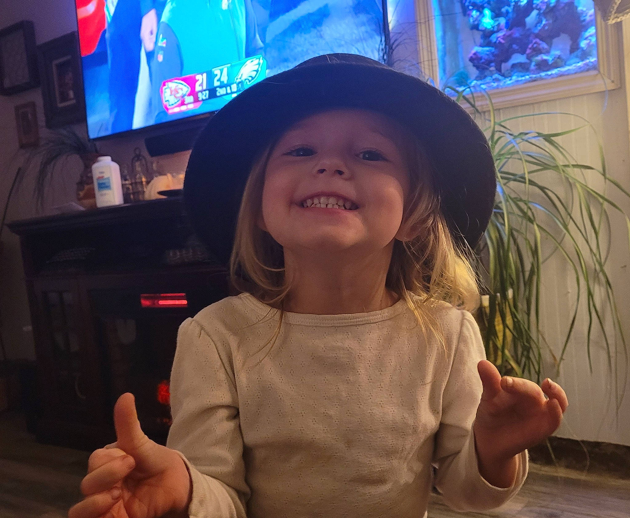 Harmony is registered to the contest to win money with this photo: arm, child, eye, facial_expression, finger, fun, gesture, hand, happy, hat, headwear, joy, organ, person, plant, smile, snapshot, standing, t_shirt, television