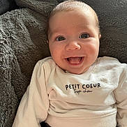 Naël participe au concours pour gagner de l'argent avec cette photo : baby, smiling, tongue_out, white_sweater, text_on_clothing, blanket, cozy, happy, cute, infant, face, portrait, clothing, soft_texture, closeup, child, indoors, light, young, person