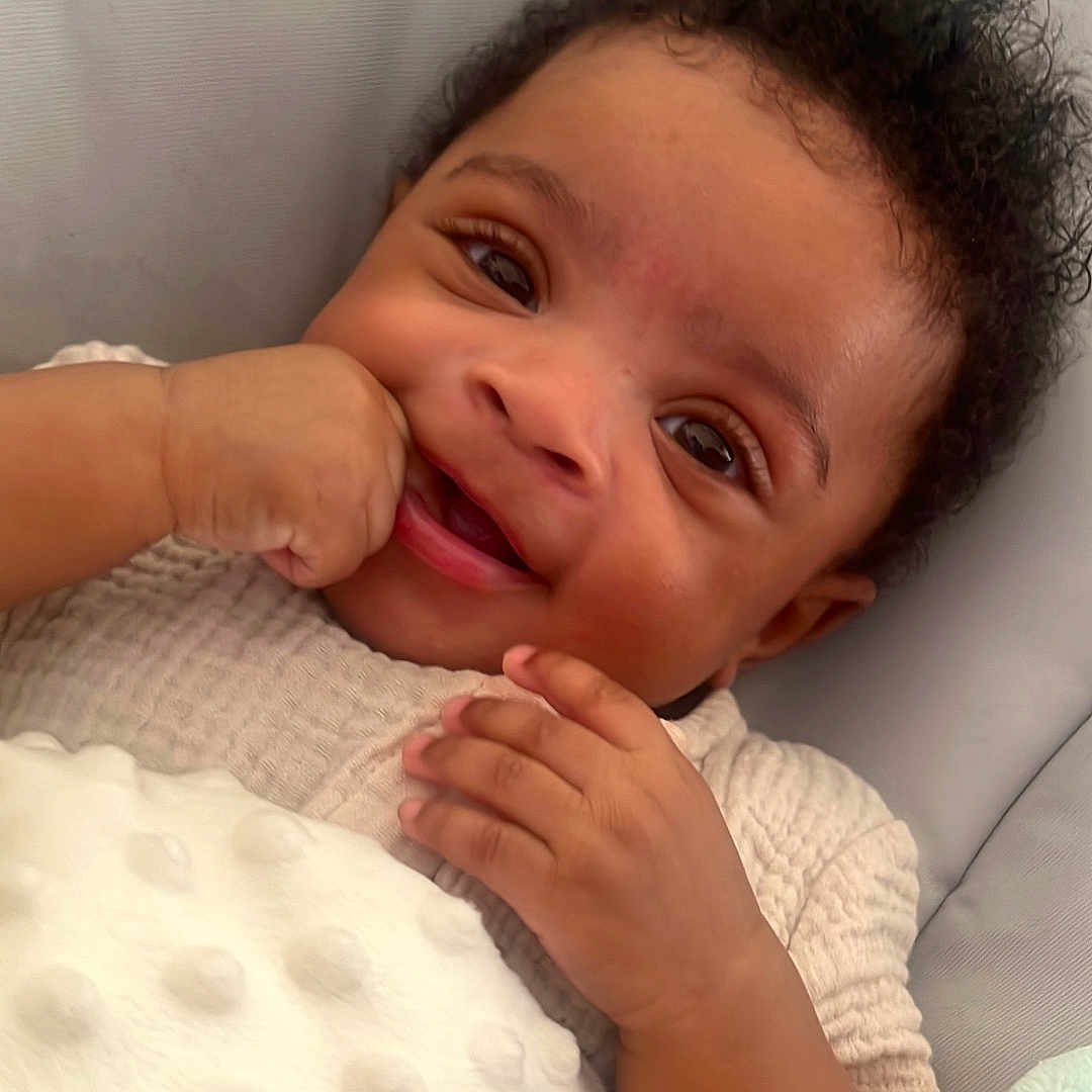 Deaudriee is registered to the contest to win money with this photo: baby, blanket, child, closeup, clothing, comfort, curly_hair, cushion, cute, expression, face, hand, happy, indoor, infant, portrait, relax, skin, smiling, soft_texture