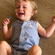 Baptiste participe au concours pour gagner de l'argent avec cette photo : toddler, child, smiling, happy, indoor, floor, wooden_floor, blue_clothing, sleeveless, pen, paper, blonde_hair, casual, portrait, young_child, cute, playful, person, baby, relaxed