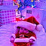 baby, infant, santa_costume, christmas_tree, christmas_lights, gifts, wrapped_presents, holiday, festive, red_clothing, white_fur_trim, hat, blanket, indoor, cute, child, celebration, holiday_decorations, smiling, festivity