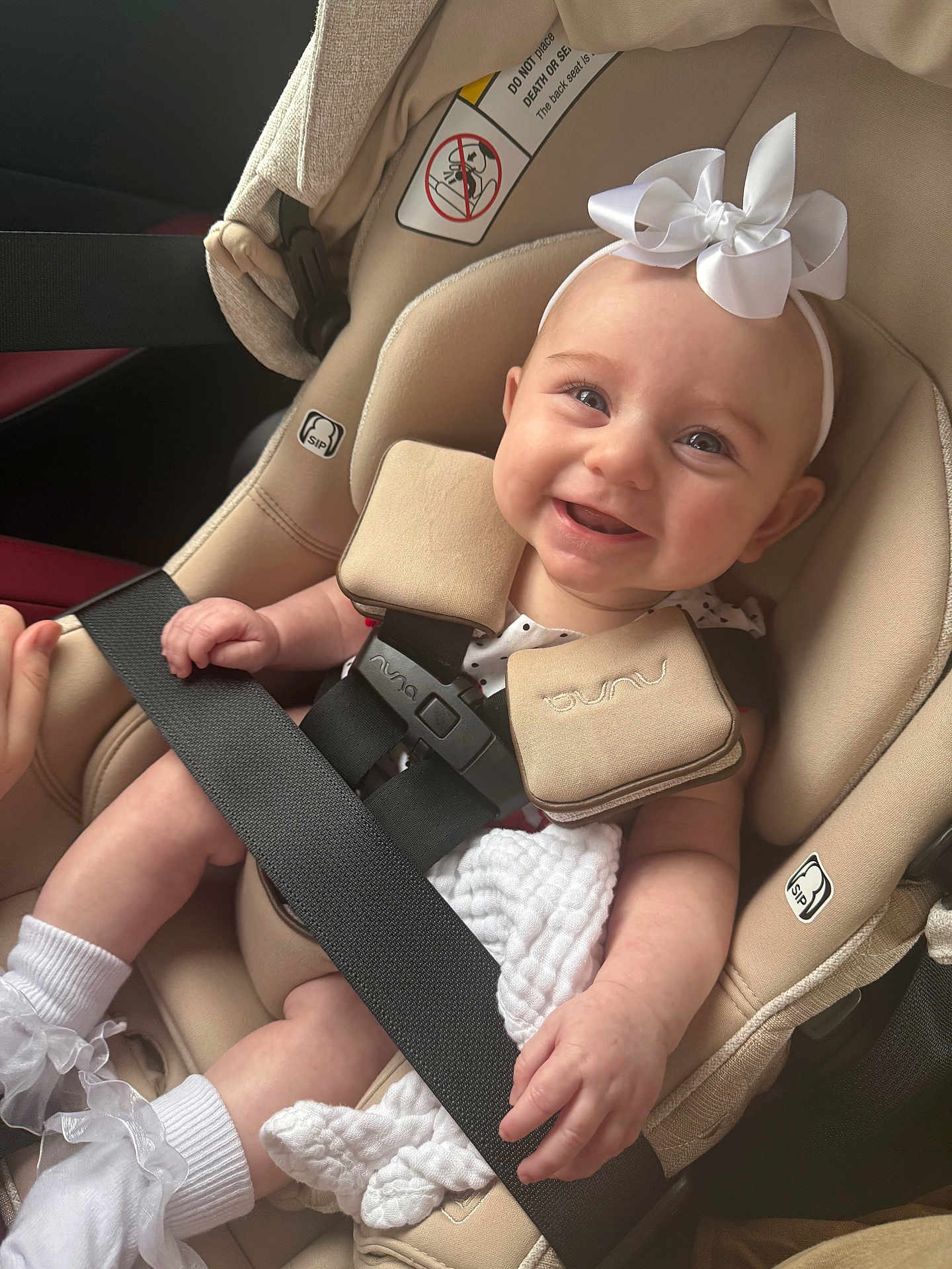 Rowan is registered to the contest to win money with this photo: baby, car_seat, smiling, white_bow, headband, infant, child, seatbelt, cute, happy, clothing, socks, blanket, sitting, safety, interior, car, person, portrait, young