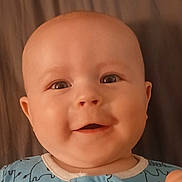 Jasper is registered to the contest to win money with this photo: baby, child, smile, face, onesie, elephant_pattern, blue_clothing, infant, happy, lying_down, closeup, cute, skin, head, eyes, mouth, indoors, soft_surface, background, portrait