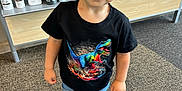 Isaiah is registered to the contest to win money with this photo: child, boy, tshirt, dinosaur, jeans, shoes, carpet, indoor, shelf, magazines, hair_products, black_tshirt, standing, cute, young_child, smiling, short_hair, clothing, retail, store