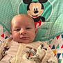 Jackson is registered to the contest to win money with this photo: baby, child, mickey_mouse, onesie, baby_seat, clothing, pattern, cartoon, indoor, portrait, smile, cute, infant, face, person, blue_socks, colorful, furniture, soft_toys, relaxing