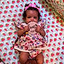 baby, infant, child, girl, floral_dress, pink_bow, bed, bedspread, patterned_bedding, wooden_sign, four_months, cute, lying_down, indoors, skin, hands, feet, portrait, curious, headband