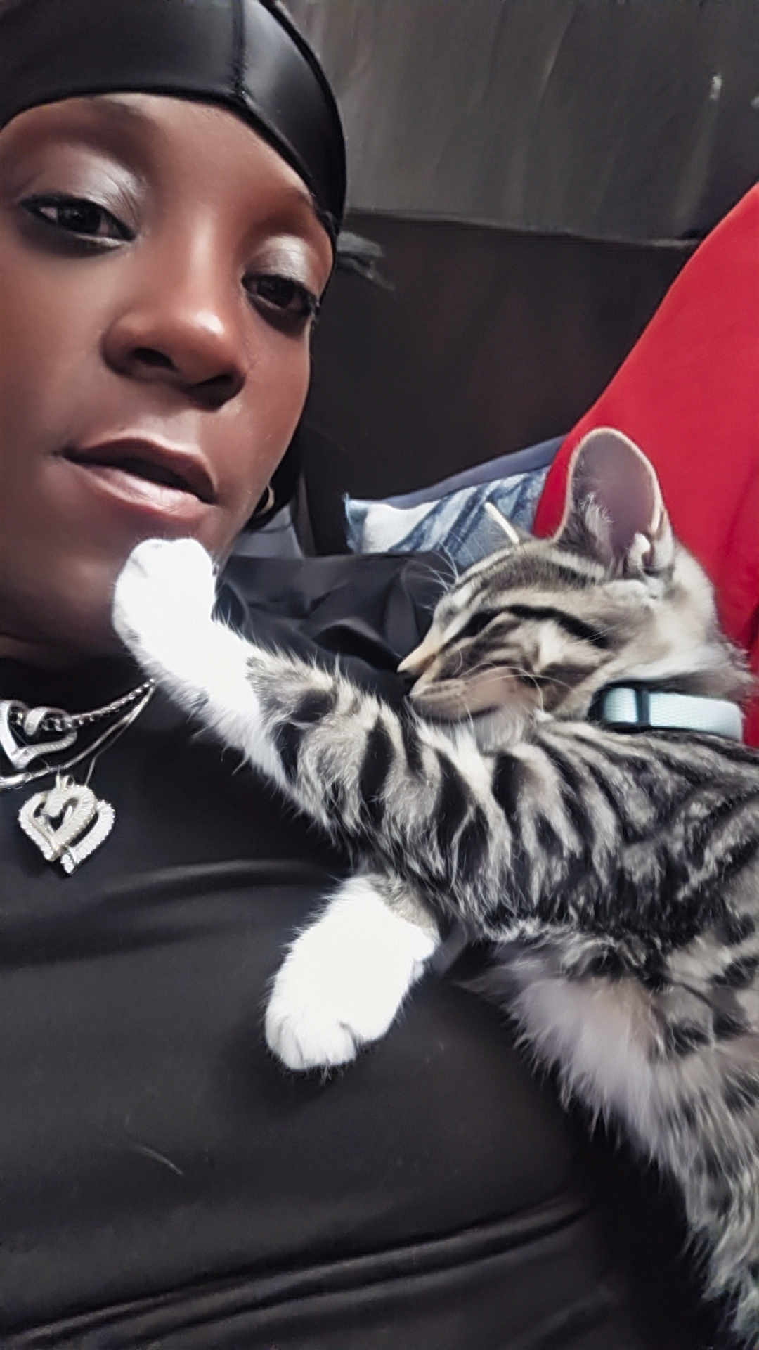 Nevaeh joined the competition — help win amazing prizes! person, cat, kitten, sleeping, closeup, portrait, black_clothing, headscarf, jewelry, necklace, heart_pendant, indoor, couch, red_cushion, affection, pet, tabby_cat, white_paws, collar, relaxation