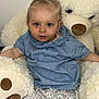 baby, bed, blue_eyes, blue_top, child, cozy, cuddly, cute, floral_shorts, furniture, indoor, infant, plush_toy, pony_tail, portrait, sitting, smiling, soft_toy, teddy_bear, white_tights