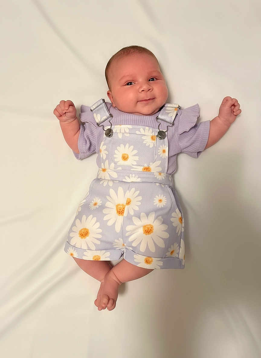 Aurora joined the competition — help win amazing prizes! baby, infant, smile, face, clothing, purple, daisy_pattern, overalls, shorts, lying_down, white_background, cute, happy, child, soft_light, skin, hands, feet, portrait, young