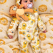 Mariam is registered to the contest to win money with this photo: baby, child, infant, portrait, lying_down, pacifier, plush_toy, stuffed_animal, onesie, hooded_outfit, lion_pattern, blanket, bedding, cozy, indoor, nursery, wide_eyed, cute, soft_toys, photography