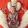 Mariam joined the competition — help win amazing prizes! baby, child, infant, portrait, smiling, sitting, headband, colorful_clothing, traditional_clothing, floral_pattern, balloons, red_background, white_fur, faux_fur, ribbons, confetti, celebration, indoor, fashion, happy