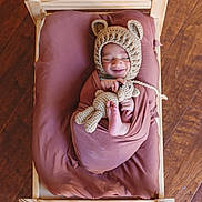 Hamza joined the competition — help win amazing prizes! baby, infant, smiling, wooden_cradle, brown_blanket, knitted_hat, bear_ears, crocheted_toy, teddy_bear, wrapped, sleeping_baby, cute, cozy, indoors, wooden_floor, child, newborn, portrait, resting, soft_texture