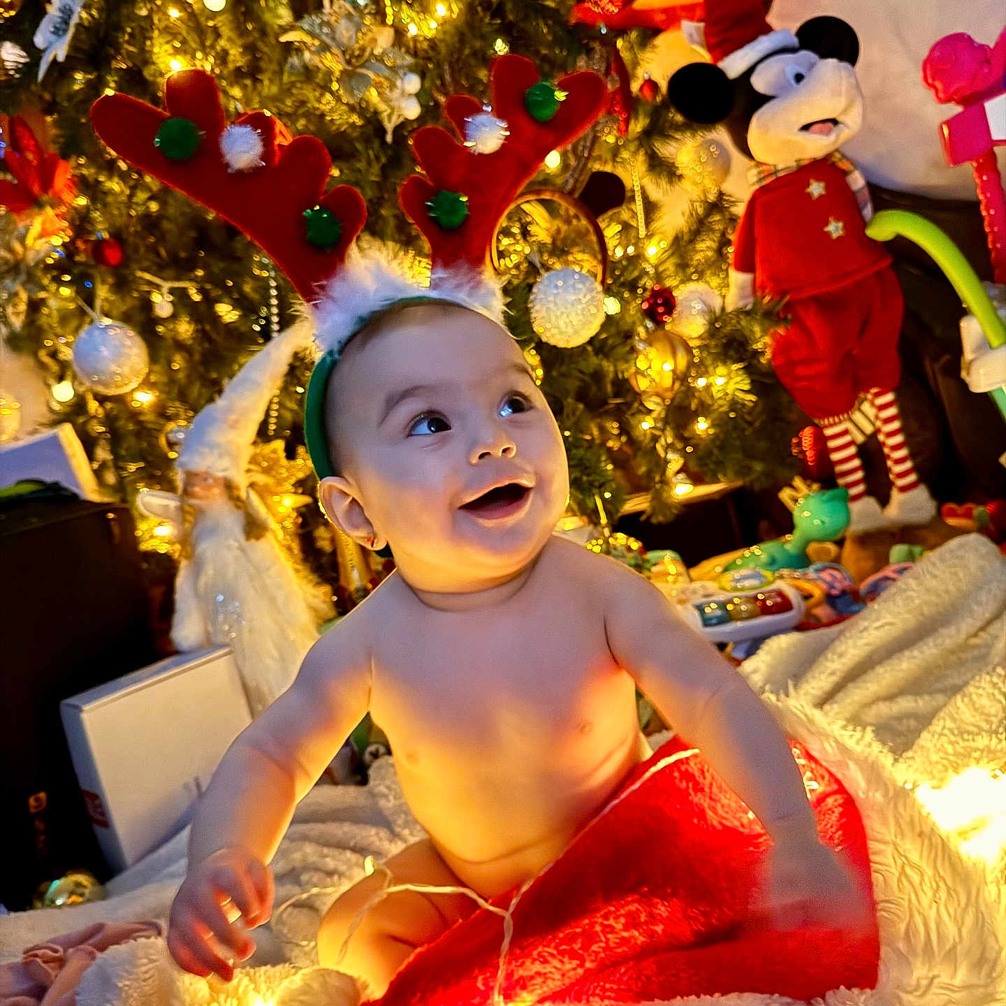 Freya joined the competition — help win amazing prizes! baby, blanket, celebration, christmas, christmas_tree, cute, decorations, festive, holiday_lights, holiday_season, indoors, infant, joyful, mickey_mouse, red_hat, reindeer_antlers, smiling, soft_texture, toy, warm_lighting
