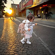 Freya joined the competition — help win amazing prizes! child, toddler, backpack, street, sunset, sidewalk, pavement, outdoor, city, walking, snack, young_child, clothing, footwear, hair_tie, pacifier, urban, light, shadow, playful