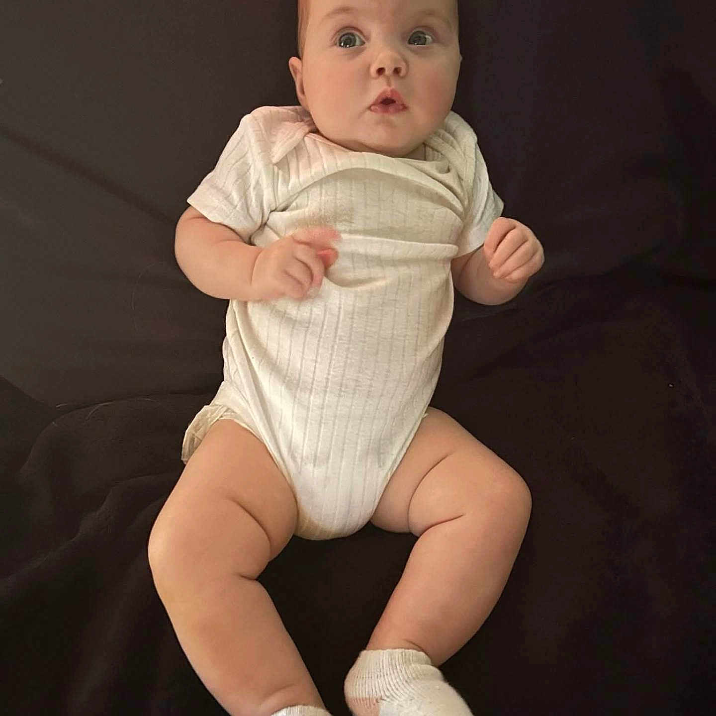 Natalie joined the competition — help win amazing prizes! baby, blanket, child, chubby, curious, cute, expression, face, feet, hands, head, indoor, infant, legs, lying_down, onesie, portrait, skin, socks, soft_lighting