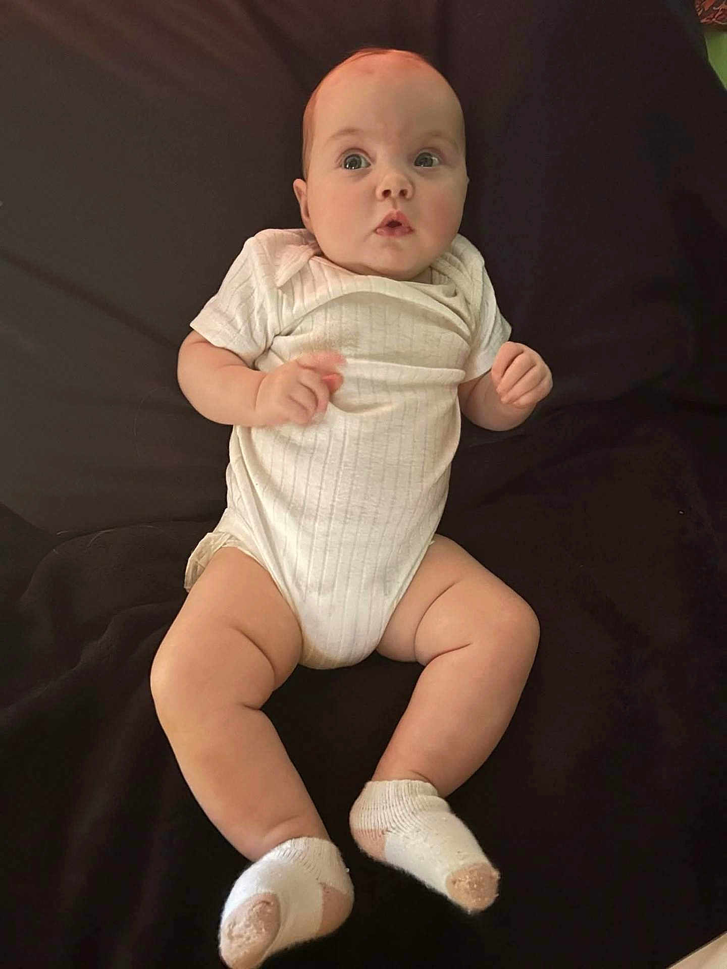 Natalie joined the competition — help win amazing prizes! baby, infant, child, onesie, socks, lying_down, curious, chubby, cute, soft_lighting, blanket, indoor, portrait, skin, hands, legs, feet, face, head, expression