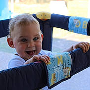 Loïs participe au concours pour gagner de l'argent avec cette photo : baby, blue, child, closeup, cute, fabric, face, fun, grip, hands, happy, indoor, infant, joyful, padded, person, playpen, portrait, smiling, young