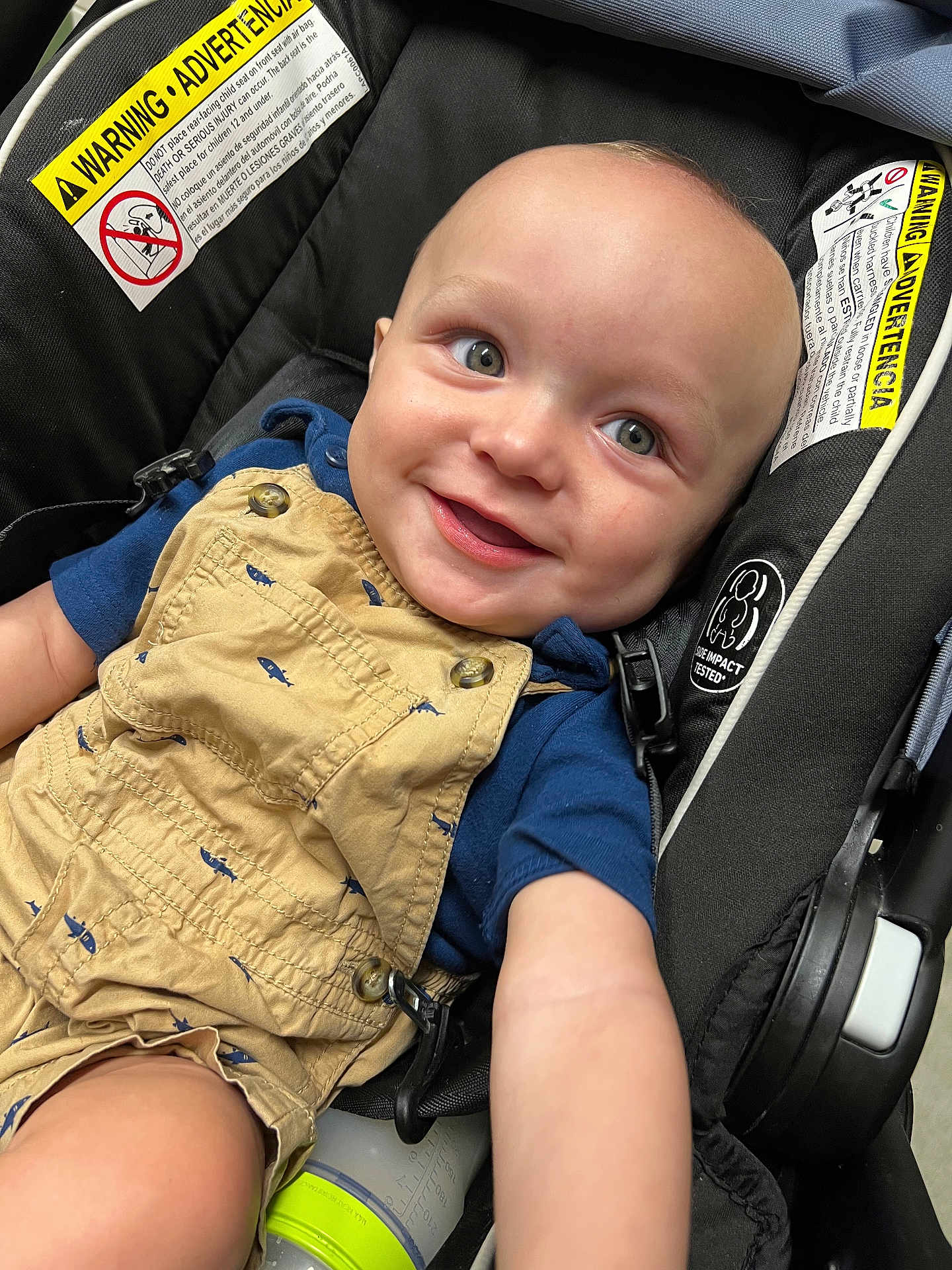 Theo joined the competition — help win amazing prizes! baby, child, smiling, car_seat, overalls, blue_shirt, baby_bottle, face, eyes, arm, clothing, seatbelt, warning_label, infant, cute, safety, indoor, person, portrait, happy