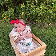 Camila joined the competition — help win amazing prizes! baby, child, smile, red_bow, headband, embroidered_dress, wooden_crate, grass, greenery, outdoor, happy, cute, sitting, nature, foliage, portrait, infant, playful, sunlight, garden