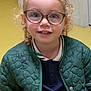 child, girl, glasses, curly_hair, green_jacket, navy_dress, smile, indoor, yellow_floor, blonde_hair, portrait, cute, young, fashion, person, happy, eyewear, casual_clothing, standing, background