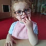 Amnnesya participe au concours pour gagner de l'argent avec cette photo : toddler, child, glasses, curly_hair, pink_bib, table, indoor, red_floor, hand, face, smiling, blue_eyes, clothing, person, portrait, cute, sitting, young_child, playful, fingers