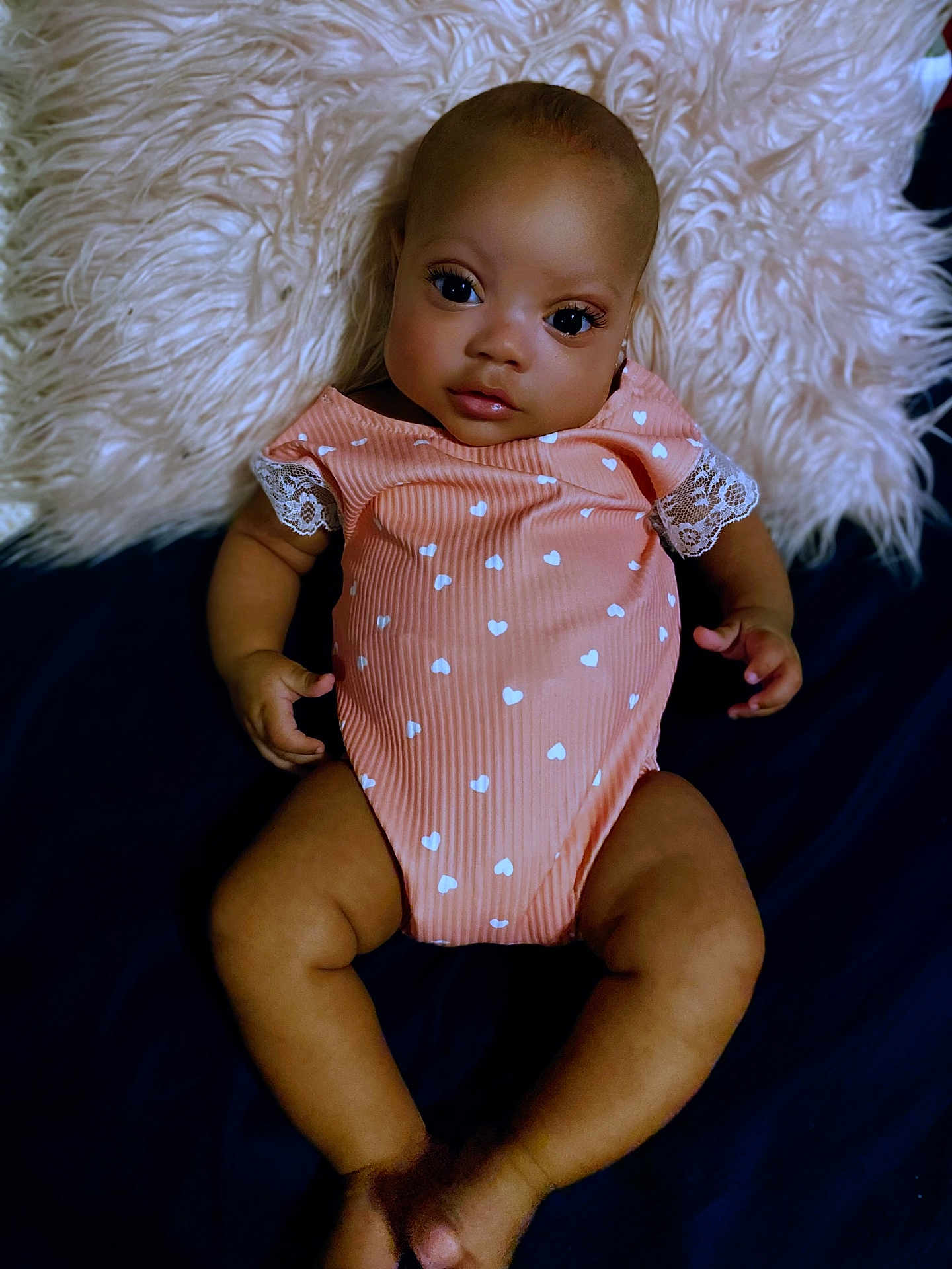 Zariah is registered to the contest to win money with this photo: baby, infant, child, onesie, heart_pattern, lace, pillow, fluffy, fabric, skin, face, eyes, hands, legs, feet, lying_down, portrait, indoor, cute, soft