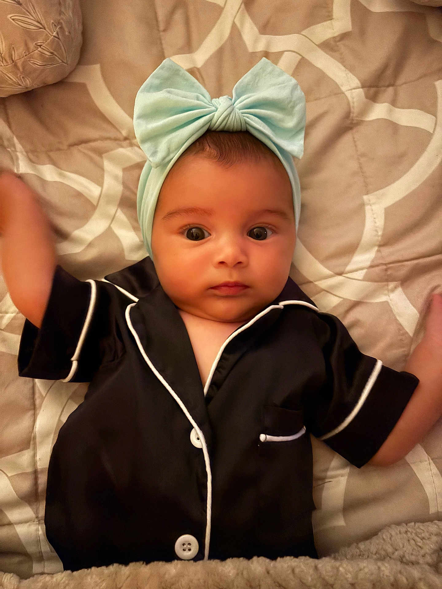 Alianna is registered to the contest to win money with this photo: baby, infant, headband, bow, pajamas, black_clothing, white_piping, bed, quilt, blanket, face, arms, wide_eyes, lying_down, indoors, soft_lighting, cute, child, person, portrait