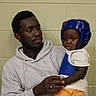 Muhammad joined the competition — help win amazing prizes! adult, child, protective_gear, helmet, chest_guard, indoor, brick_wall, person, holding, casual_clothing, hoodie, curious, serious, portrait, safety, interaction, family, black_hair, close_up, expression